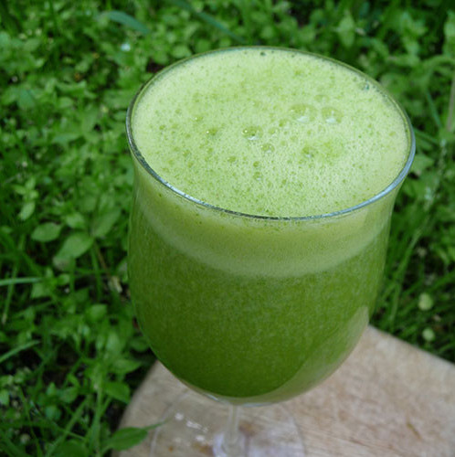 A glass full of juice with chickweed in the background