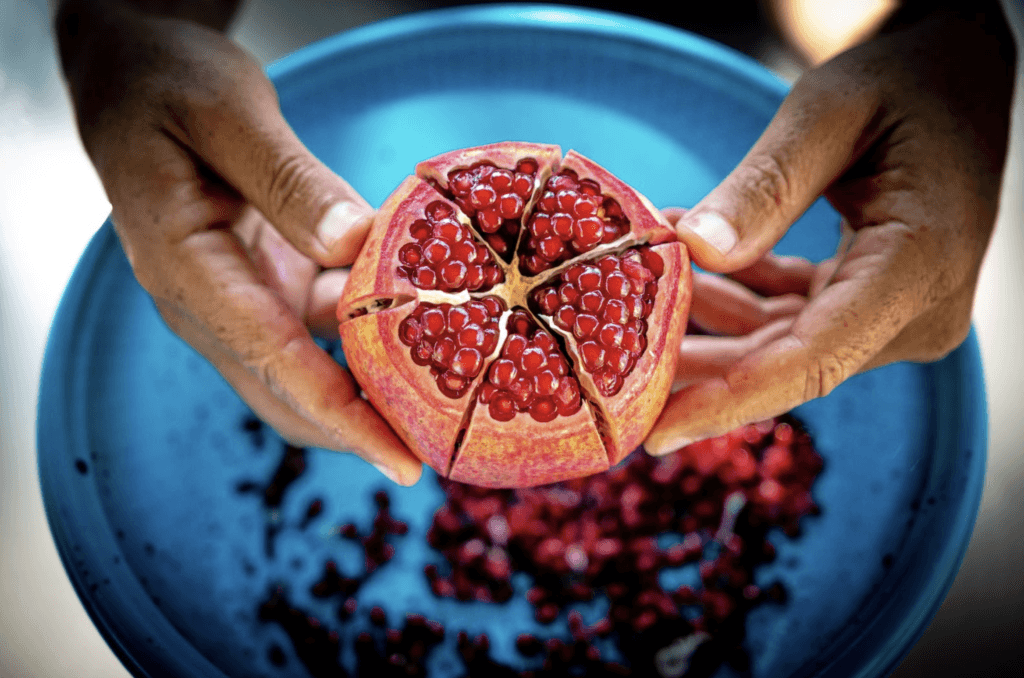 Person holds an open cut pomegranate in his hand over a blue bowl