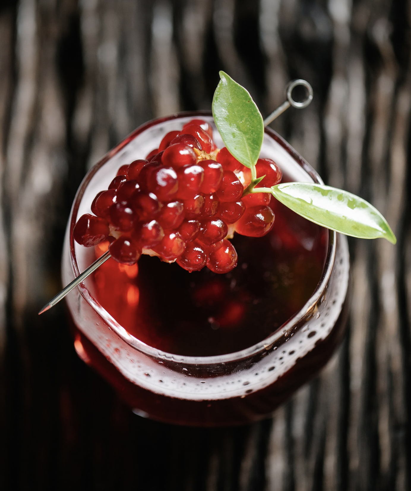 The picture shows a glas of pommegrante juice with some fruits on a pick laying on top